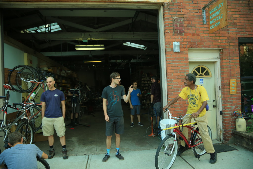 John Martin (center), the Bradley Street Bicycle Co-op's founder, and Joe Comfort (right), a regular, outside the shop. (Credit to Will Reid)